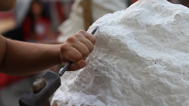 Young student at work learning craftsman profession in art class, working with hammer to carving stone statue from white stone