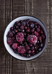 Frozen berries mix in a black bowl on wooden background