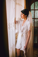 Beautiful bride in robe posing near window, wedding preparation