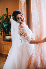 Portrait of beautiful bride with fashion veil posing on bed at window