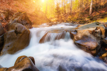 Beautiful fall scene  of mountain river with waterfall and rapids at sunlight.