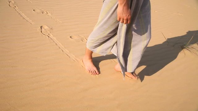 A man walks barefoot on the desert. Visible only to the legs