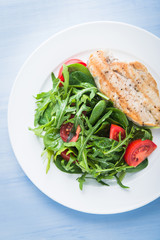 Fototapeta na wymiar Roasted chicken breast and fresh salad with tomato and greens (spinach, arugula) top view on blue wooden background. Healthy food.