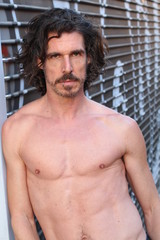 Naklejka premium Handsome man with long hair and beard. He is posing in front of camera just with open jeans and showing his muscles. Abdominal dominant part.