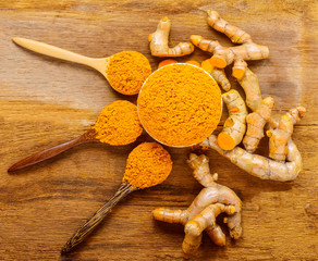Turmeric roots with turmeric powder on wooden background