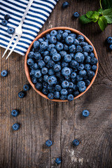 Full bowl of fresh ripe blueberries on old wooden board