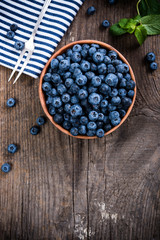 Full bowl of fresh ripe blueberries on old wooden board