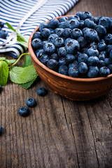 Full bowl of fresh ripe blueberries on old wooden board