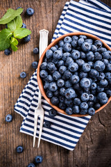 Full bowl of fresh ripe blueberries on old wooden board
