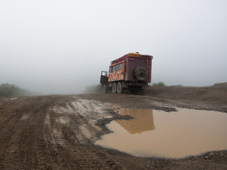 Military freight car standing on a dirt road with puddle on a background of fog