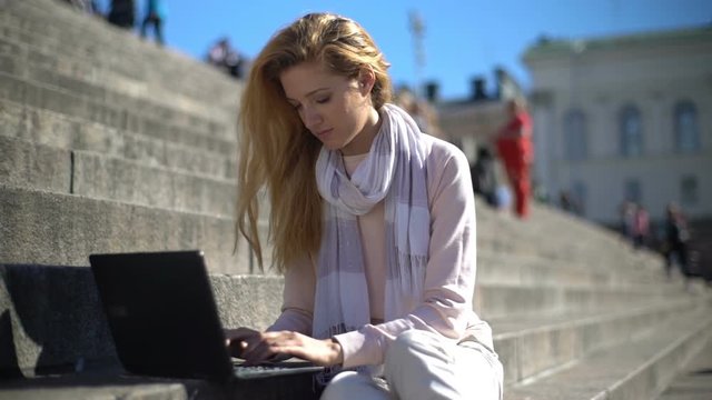 Young woman uses a laptop on the stairs in the center of the city. Slow motion.