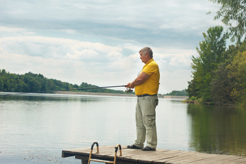 Senior man in yellow shirt standing and fishing from the old wooden dock