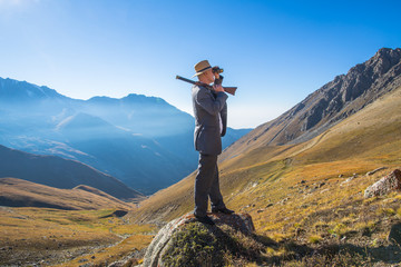 a man in a suit and with a gun on a background of mountains in the summer, panorama, landscape,...