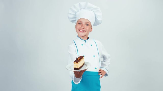 Baker enter the frame with chocolate biscuit and gives you it. Chef 7-8 years smiling at camera. Isolated on white background. Thumb up. Ok