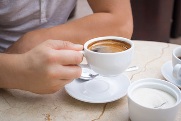 Man at table holds cup of americano coffee