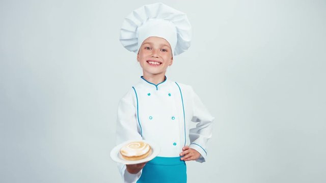 Baker enters the frame holding plate with little cream cake and gives you it. Chef 7-8 years smiling at camera. Isolated 