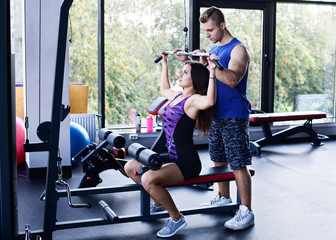 Young athletic woman doing pull down exercise for the back under a personal trainer's supervision