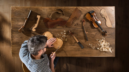 Top view. Artisan luthier working on the creation of a violin - obrazy, fototapety, plakaty