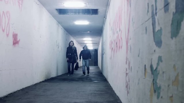 woman walking in a underground tunnel,thief mugger robber following her then runs and robs her taking her bag
