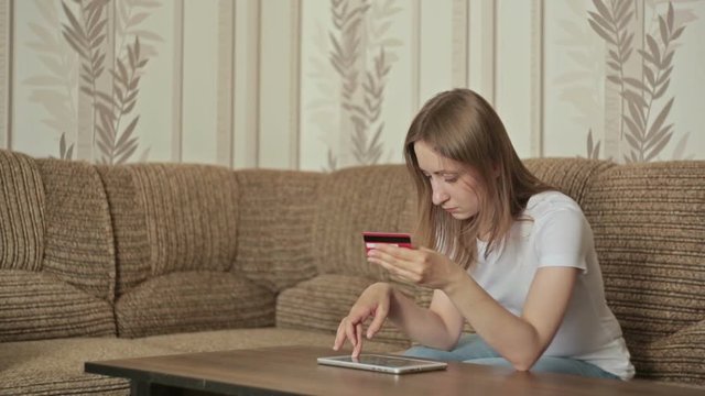 home, online, technology and internet concept - woman sitting on the couch with tablet pc and bying on internet with credit card. Female entering number security code