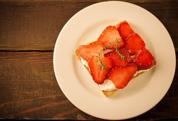 Toasted bread with cream cheese, strawberries and thyme on wooden table