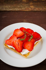 Toasted bread with cream cheese, strawberries and thyme on wooden table
