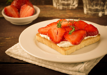 Toasted bread with cream cheese, strawberries and thyme on wooden table