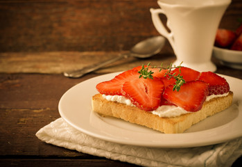 Toasted bread with cream cheese, strawberries and thyme on wooden table