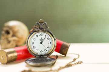 Still life antique clock placed on a wooden floor and a red shotgun shell with human skull on the back.