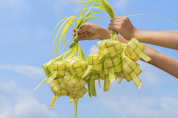 A hand holding Ketupat - Malay cuisine made from glutinous rice packed inside a diamond shaped container of wooven palm leaf.