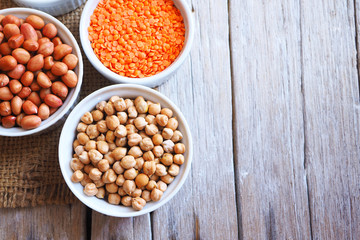 Top view of chickpeas, peanuts and red lentils on a wooden table.