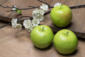 Granny Smith apples and blossom on wood board.