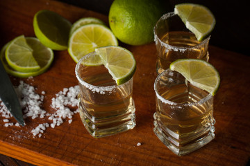 Macro photo of shots of gold Mexican tequila with lime and salt on wooden rustic background....