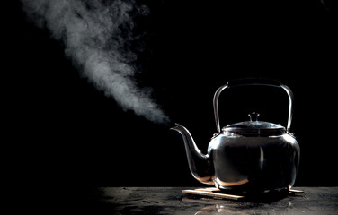 Tea kettle with boiling water on a black background