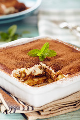 Tiramisu cake in an oven pan on a blue wooden  table with dishes and forks