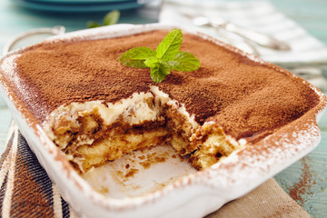 Tiramisu cake in an oven pan on a blue wooden  table with dishes and forks
