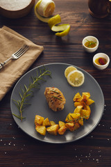 A chiken roll roasted on a gray plate with baked potatoes. low key style.