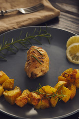 A chiken roll roasted on a gray plate with baked potatoes. low key style.