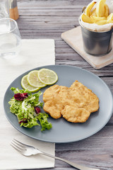 Fried chicken breast fillet on a gray plate with fries. Country style