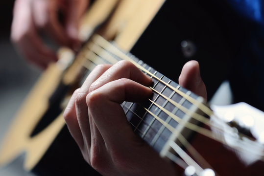 man's hands playing acoustic guitar