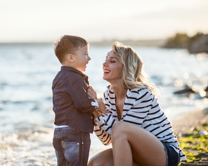 Beautiful boy with a woman relaxing on the beach. Throw pebbles into the sea, running, jumping,...