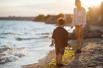 Beautiful boy with a woman relaxing on the beach. Throw pebbles into the sea, running, jumping,...