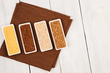 Various groats in bowls and table-napkin on white wooden table