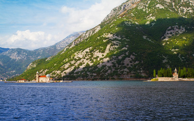 Fototapeta premium Fjord in Adriatic Sea. Our Lady of the Rock island and Church in Perast on shore of Boka Kotor bay (Boka Kotorska), Montenegro, Europe. Kotor Bay is a UNESCO World Heritage Site