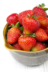 Fresh organic strawberries in bowl on white wooden background