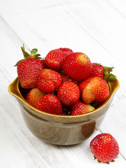 Fresh organic strawberries in bowl on white wooden background