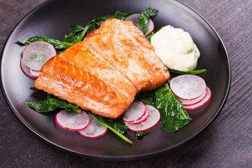 Broiled salmon with radish and spinach, served on black plate