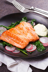Broiled salmon with radish and spinach, served on black plate. View from above, top studio shot