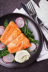 Broiled salmon with radish and spinach, served on black plate. View from above, top studio shot