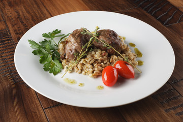 Veal (beef) cheeks with pearl barley porridge and greens in a white plate. Wooden background.